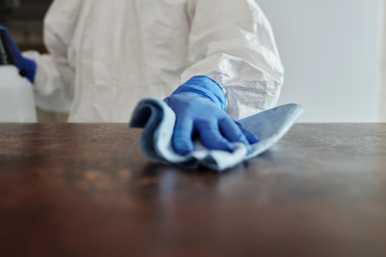 A person wearing a protective suit is wiping a wooden surface with a piece of cloth